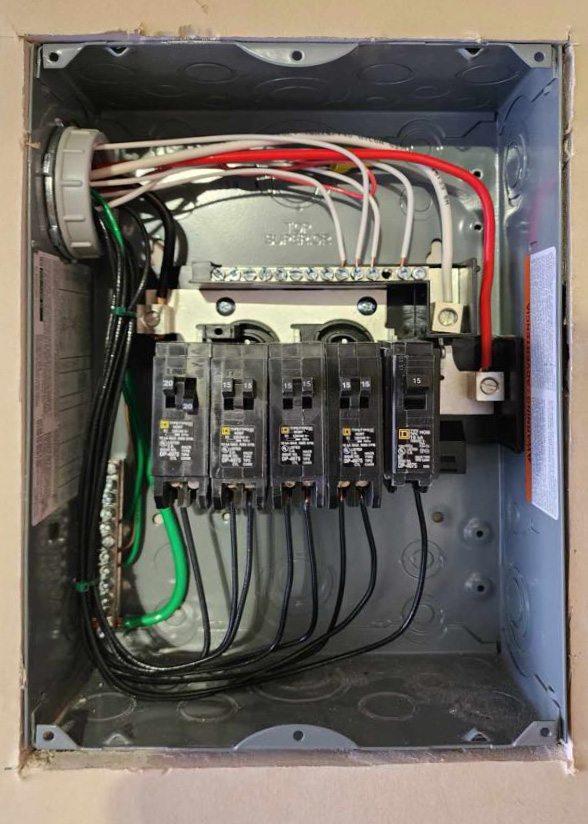 An open electrical panel with multiple circuit breakers, wires of different colors, and various electrical components visible.