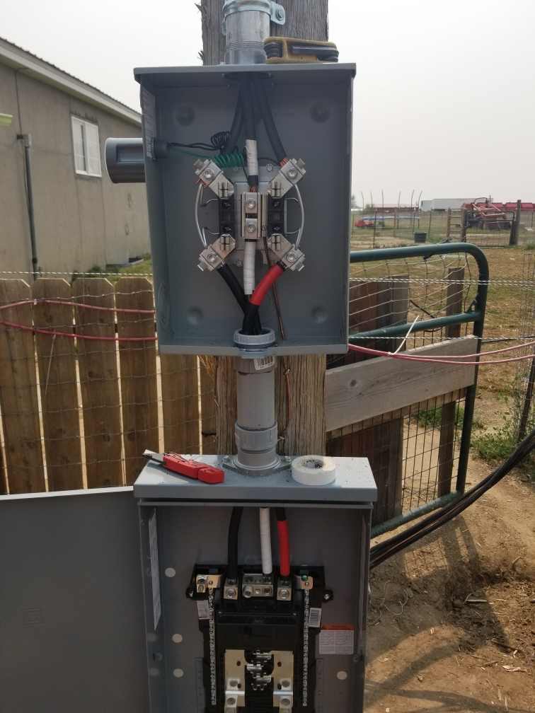 An outdoor electrical panel attached to a wooden post, with cables and connectors, against a hazy background.