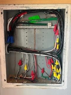 Open electrical panel with neatly organized wires secured by colorful plastic clips, mounted on a metal backing inside a white frame.