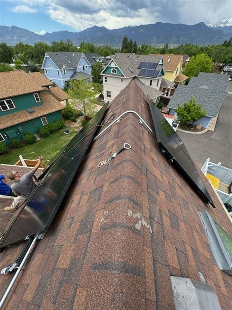 Workers install solar panels on the roof of a house in a suburban neighborhood with a mountainous backdrop.